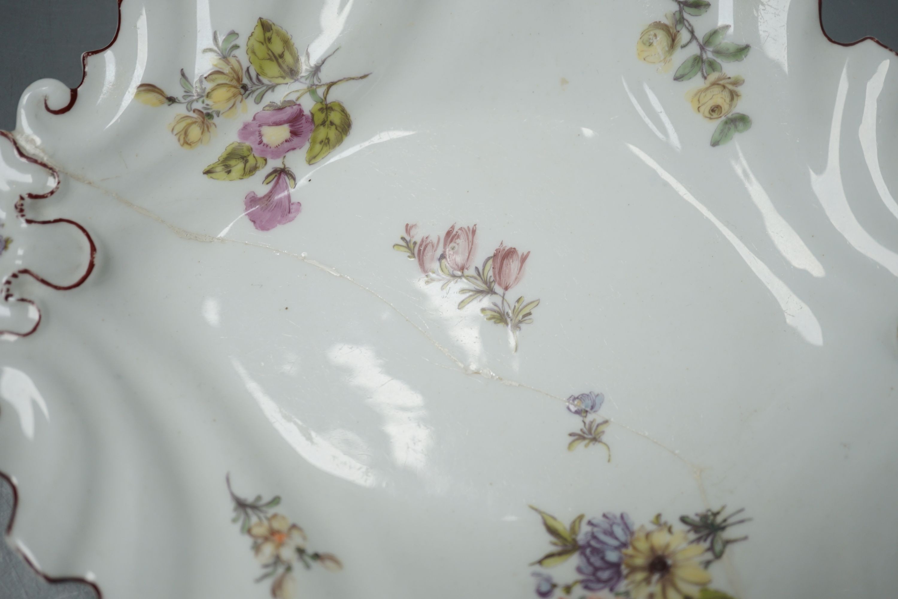 A Chelsea silver shaped dish painted with scattered English flowers under a brown line rim, red anchor and stilt marks c. 1755, 21 cms wide.